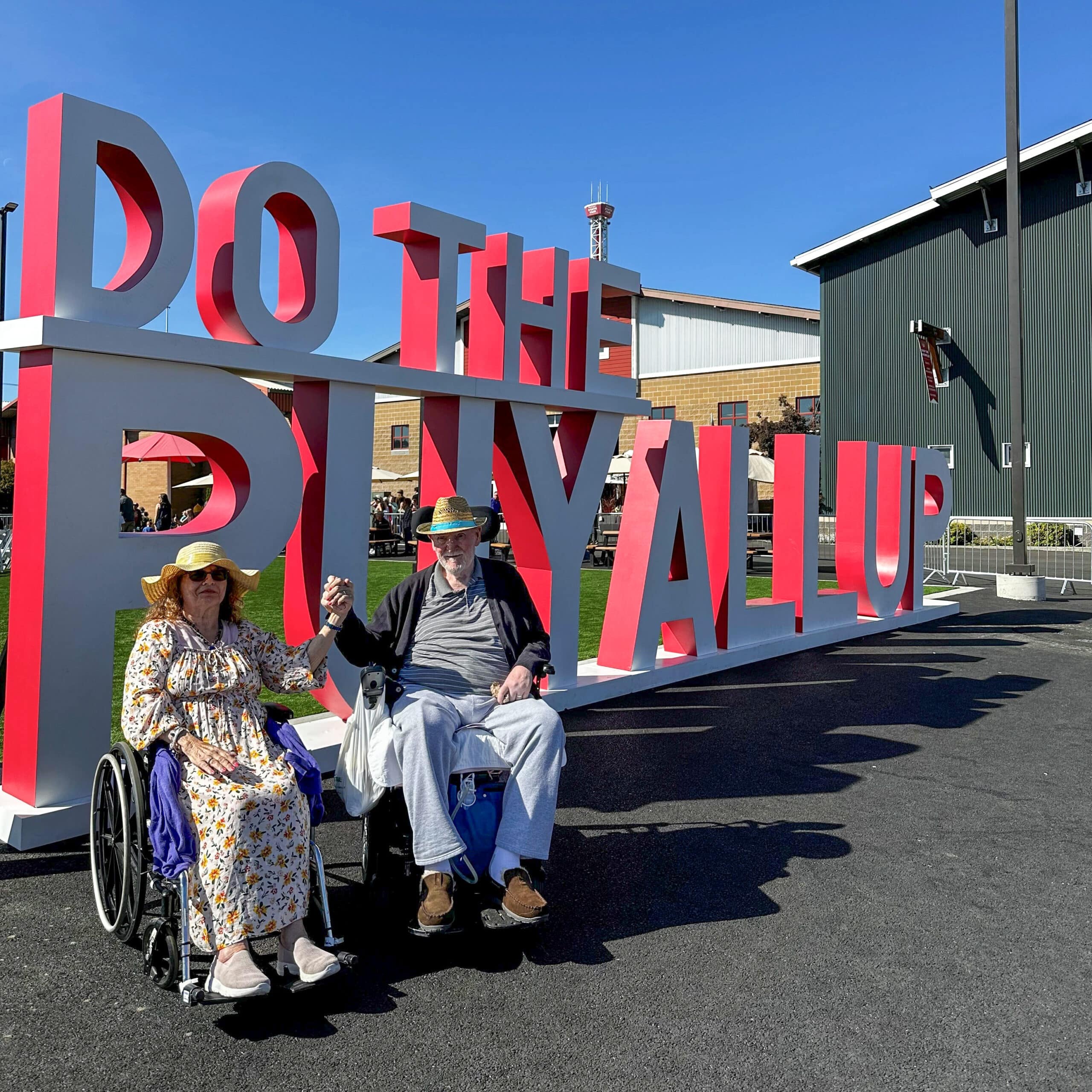 Man and woman sitting in front of a sign at a local fair.