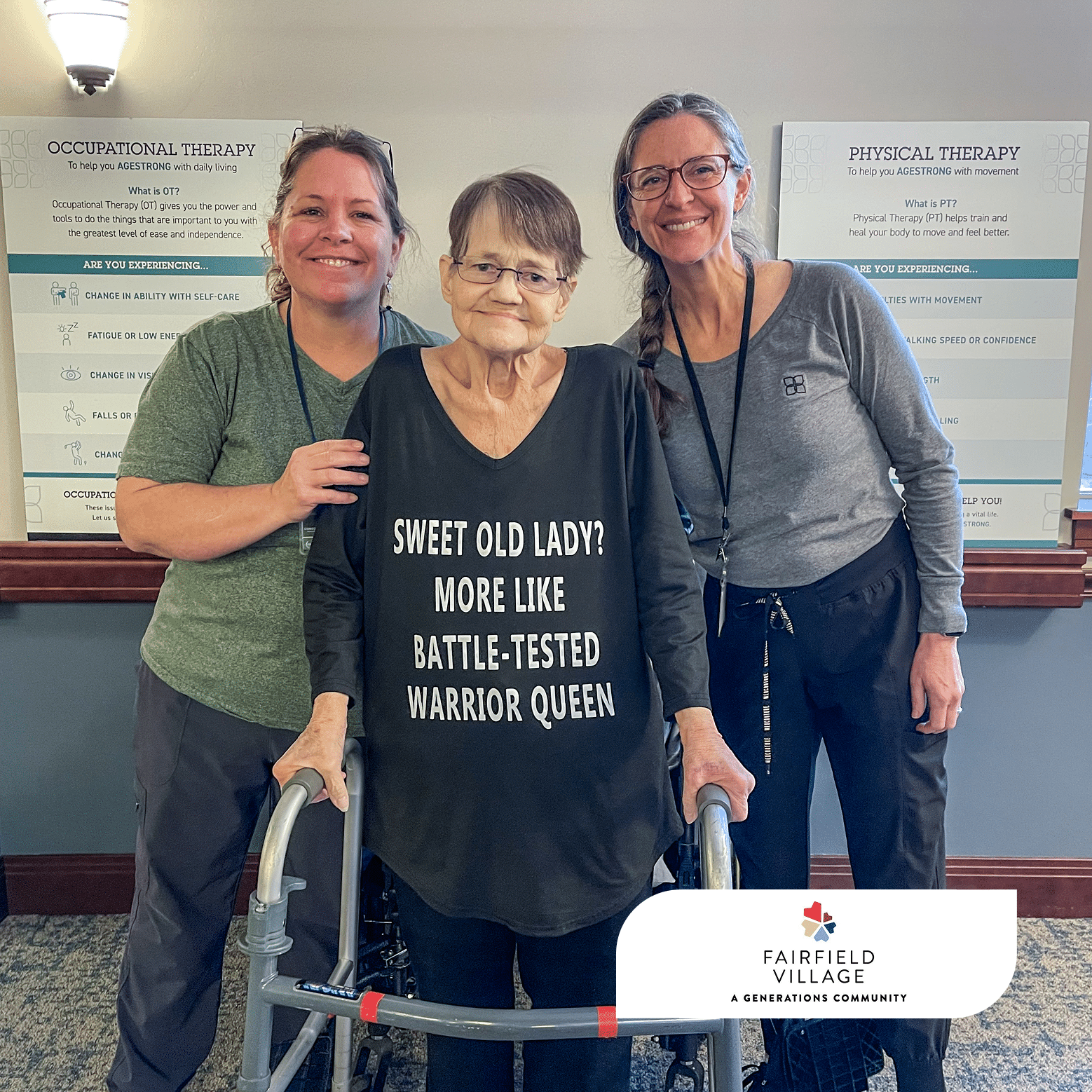 A resident stands smiling with her walker between her occupational therapist and physical therapist at Fairfield Village. She is wearing a black shirt that reads, "Sweet old lady? More like battle-tested warrior queen," while all three smile at the camera in the therapy gym, celebrating her recovery and return home.